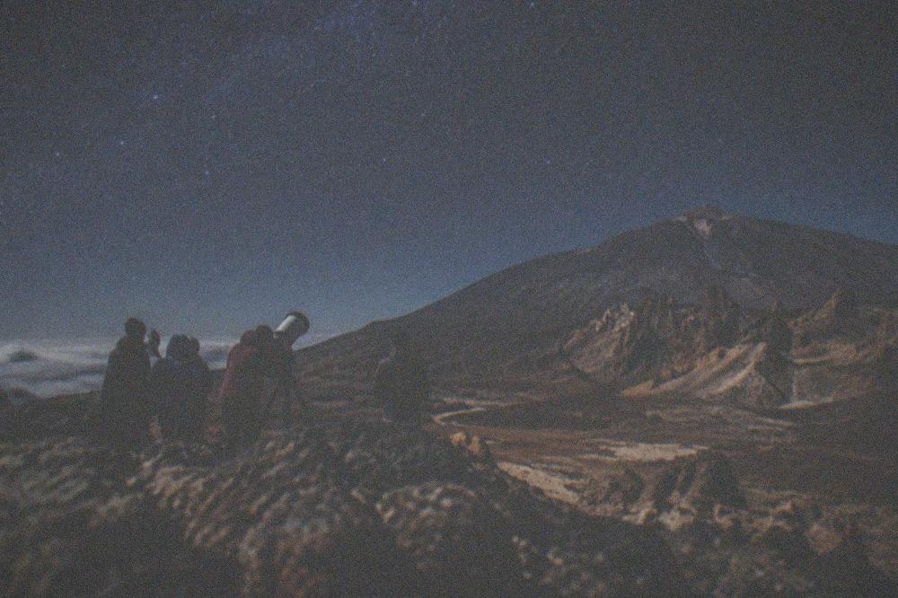 Stargazers in warm jackets gathered around a telescope at a mountain viewpoint at dusk