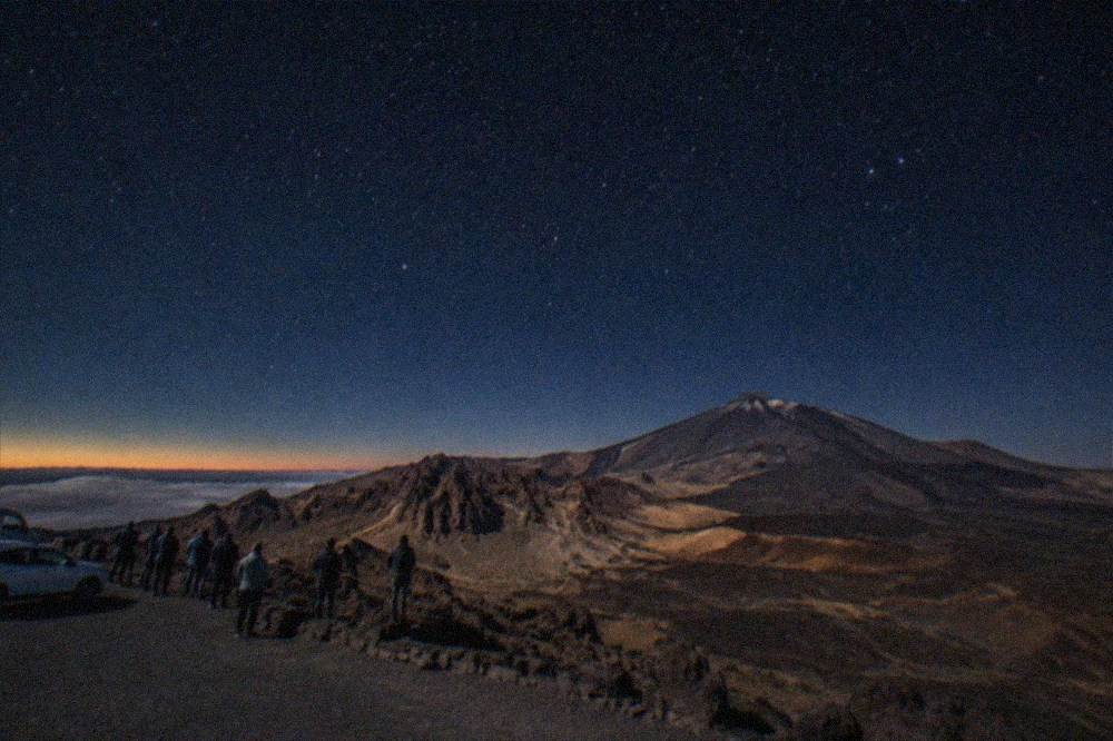 A car park viewpoint on the Teide ridge with a small crowd waiting for darkness after sunset