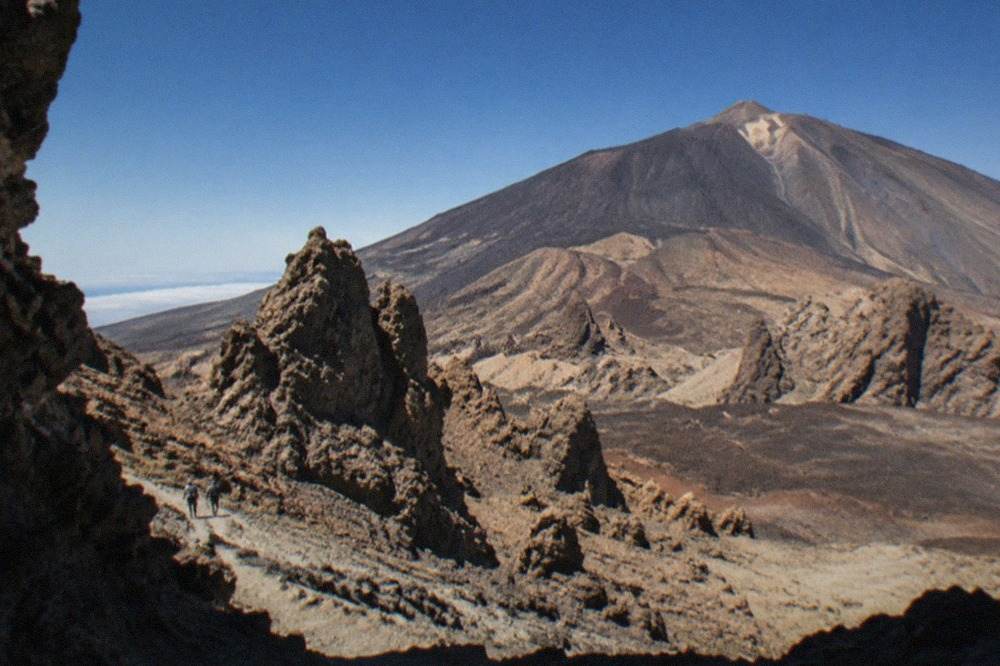 The rocky upper slopes of Mount Teide above reddish volcanic rock under a clear sky