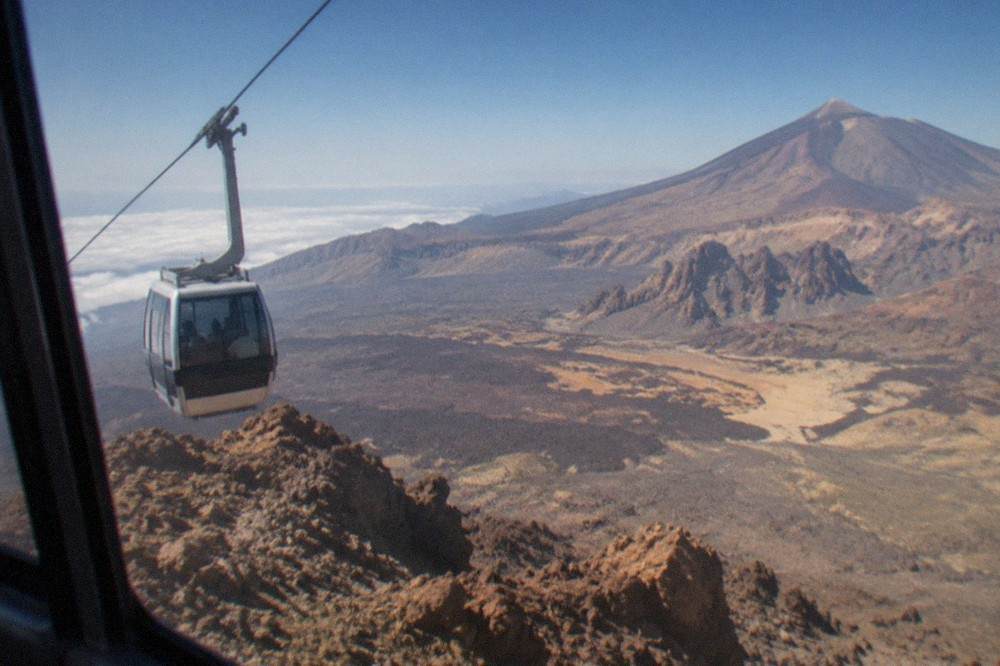 A cable car cabin travelling up the slope toward rocky peaks above the clouds