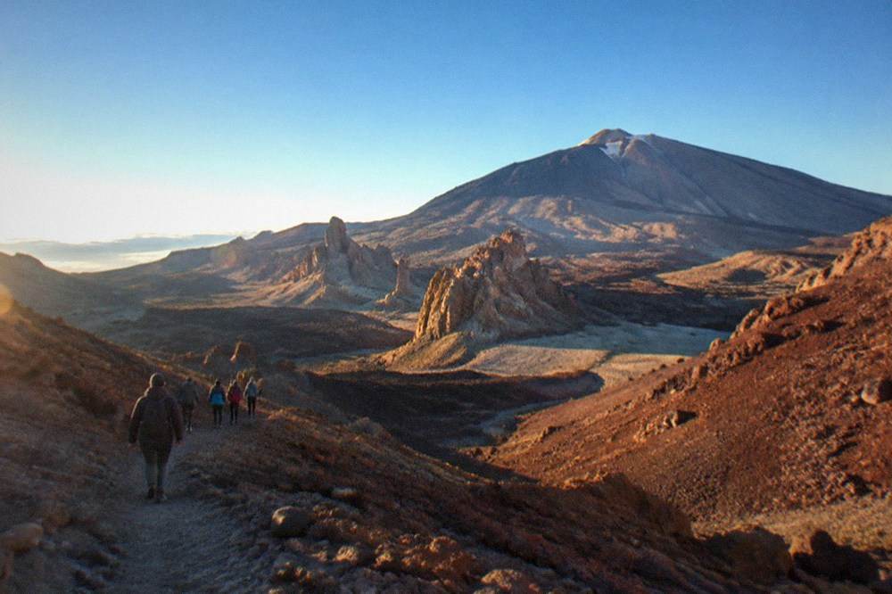 A group of walkers on a rocky trail high on the volcano with red rock slopes around them