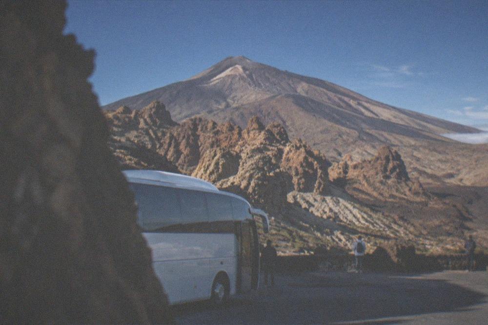 A coach parked at a volcanic viewpoint with reddish rock formations and a clear sky