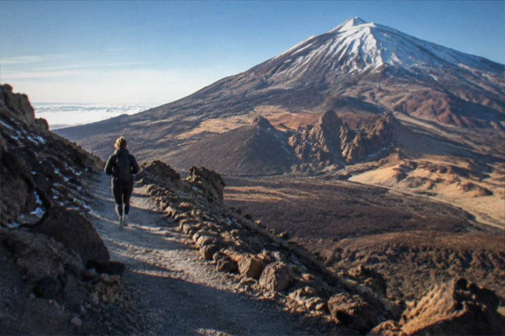 A snow-dusted volcanic slope under a blue winter sky with a path visible