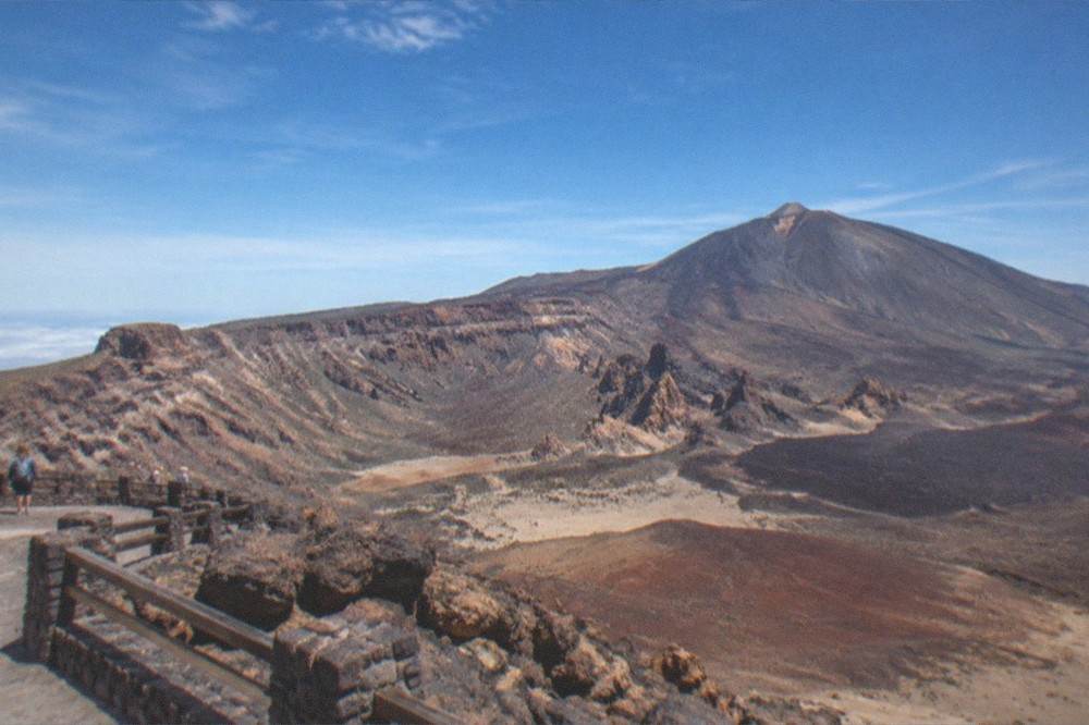 A viewpoint platform overlooking a wide volcanic caldera with layered rock slopes