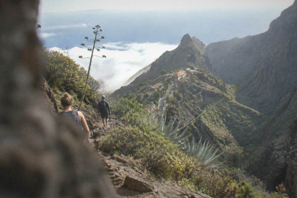 Hikers with backpacks walking a rocky path above clouds on a volcanic slope