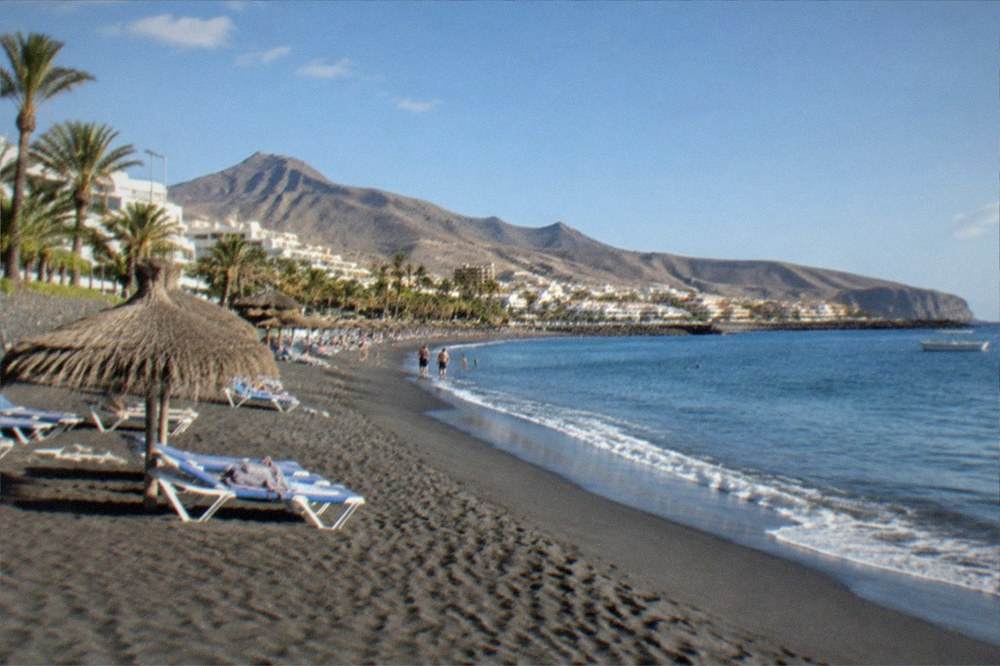 A wide sandy beach with calm water and sunbeds under a clear sky