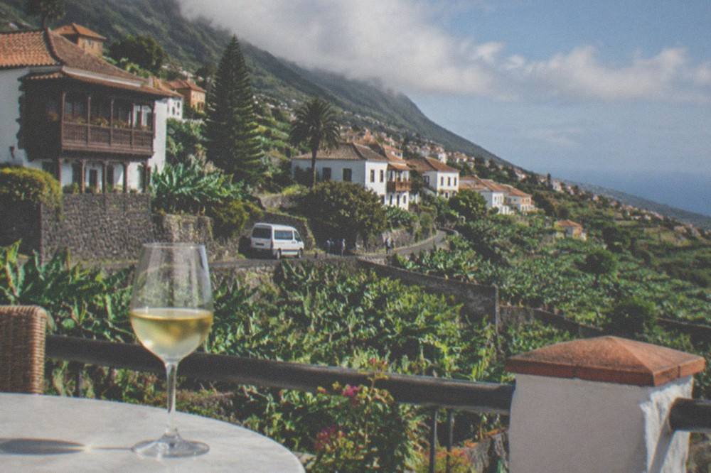 A glass of white wine on a terrace overlooking green hills and the sea