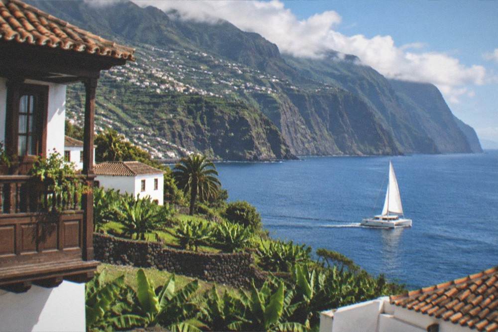 A catamaran under way on calm blue water near tall cliffs