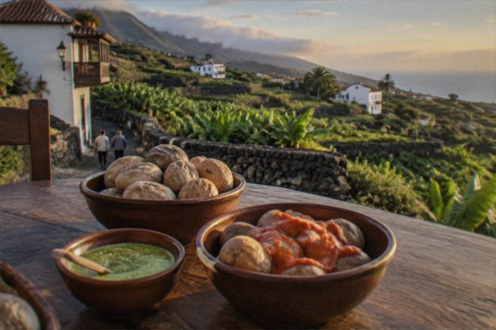 Bowls of wrinkled potatoes with red and green mojo sauces on a rustic table